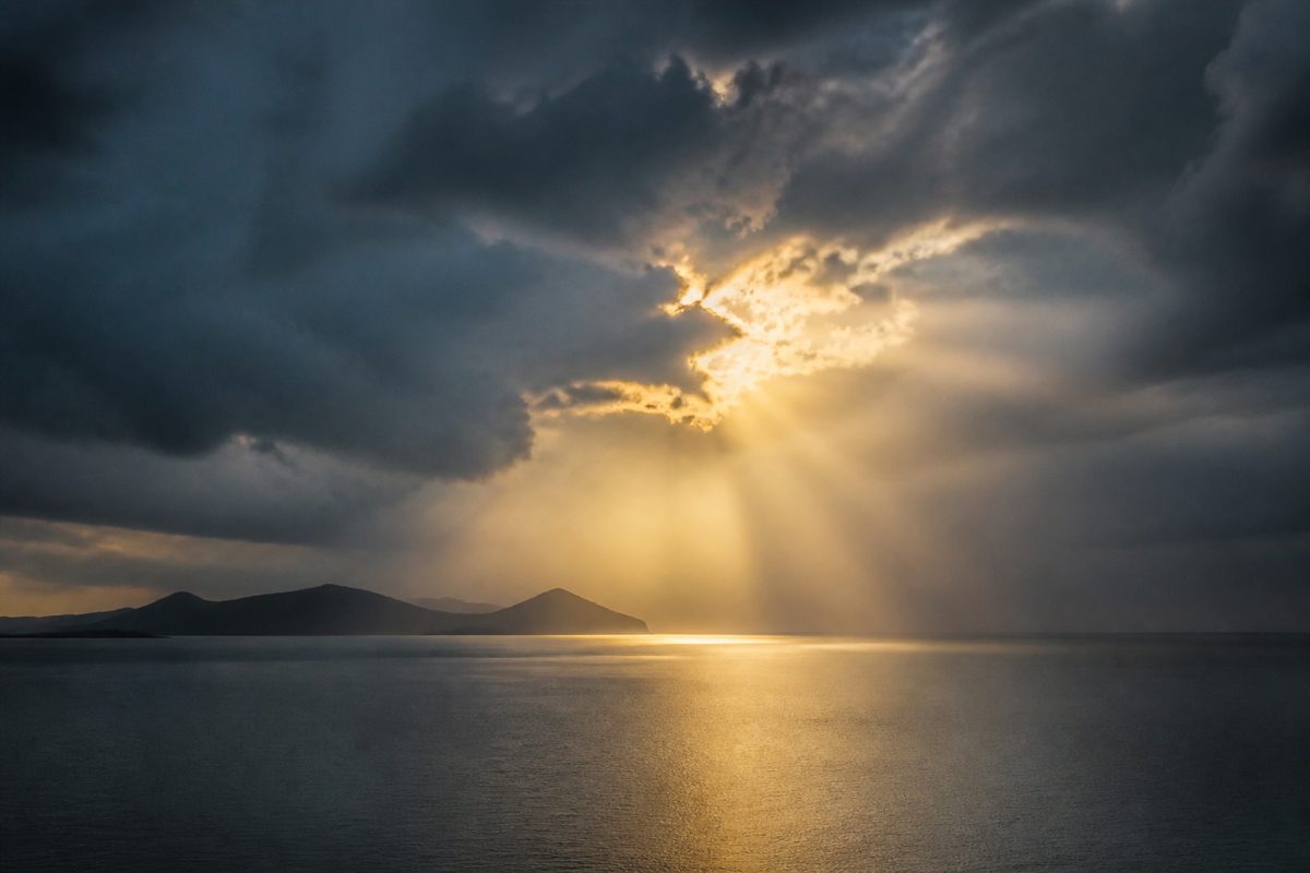 Sunlight breaking through storm clouds over calm water